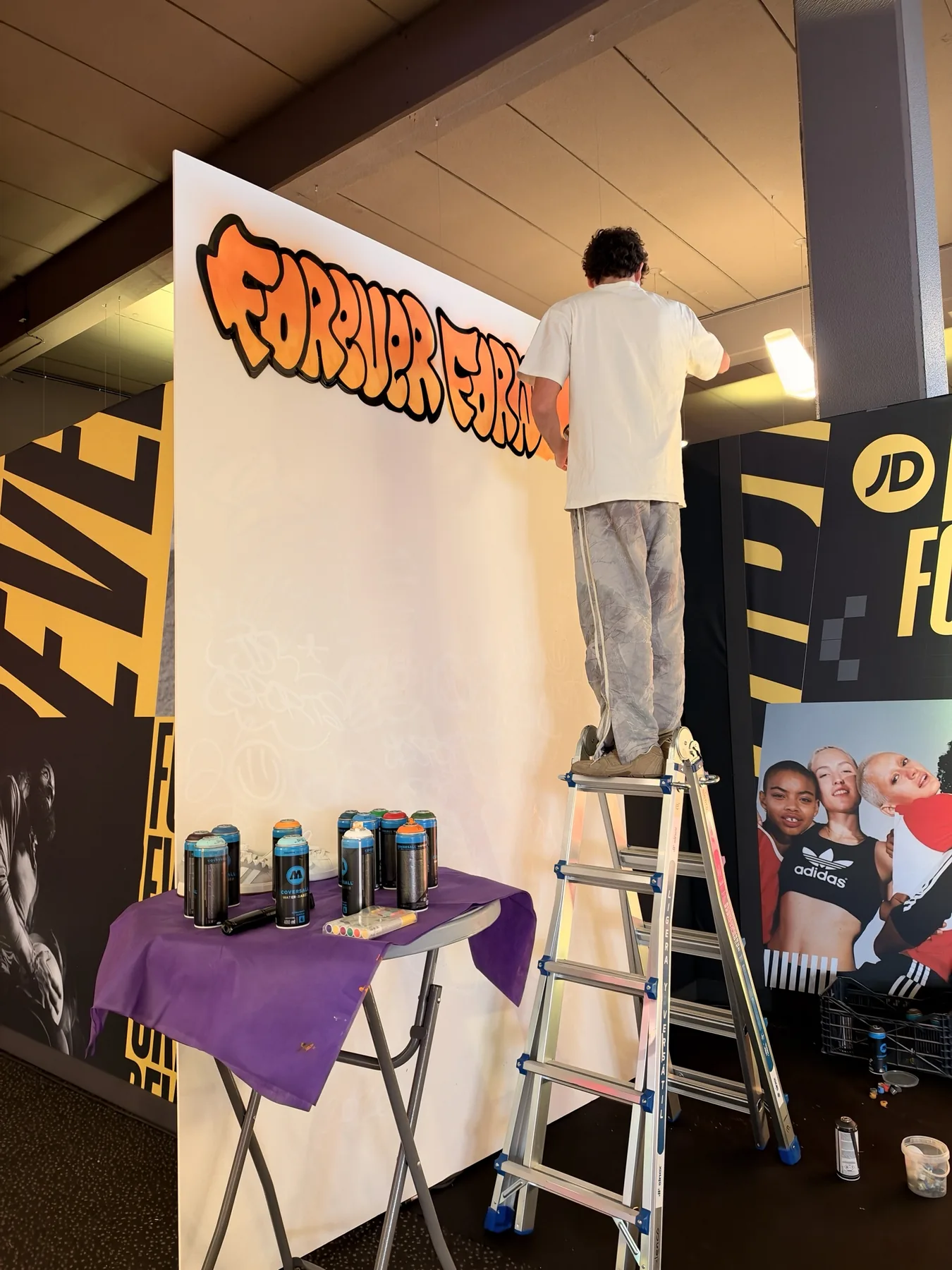 Artista de Dale Color pintando en directo con spray el lettering «Forever Forward» sobre el lienzo del stand de JD Sports.