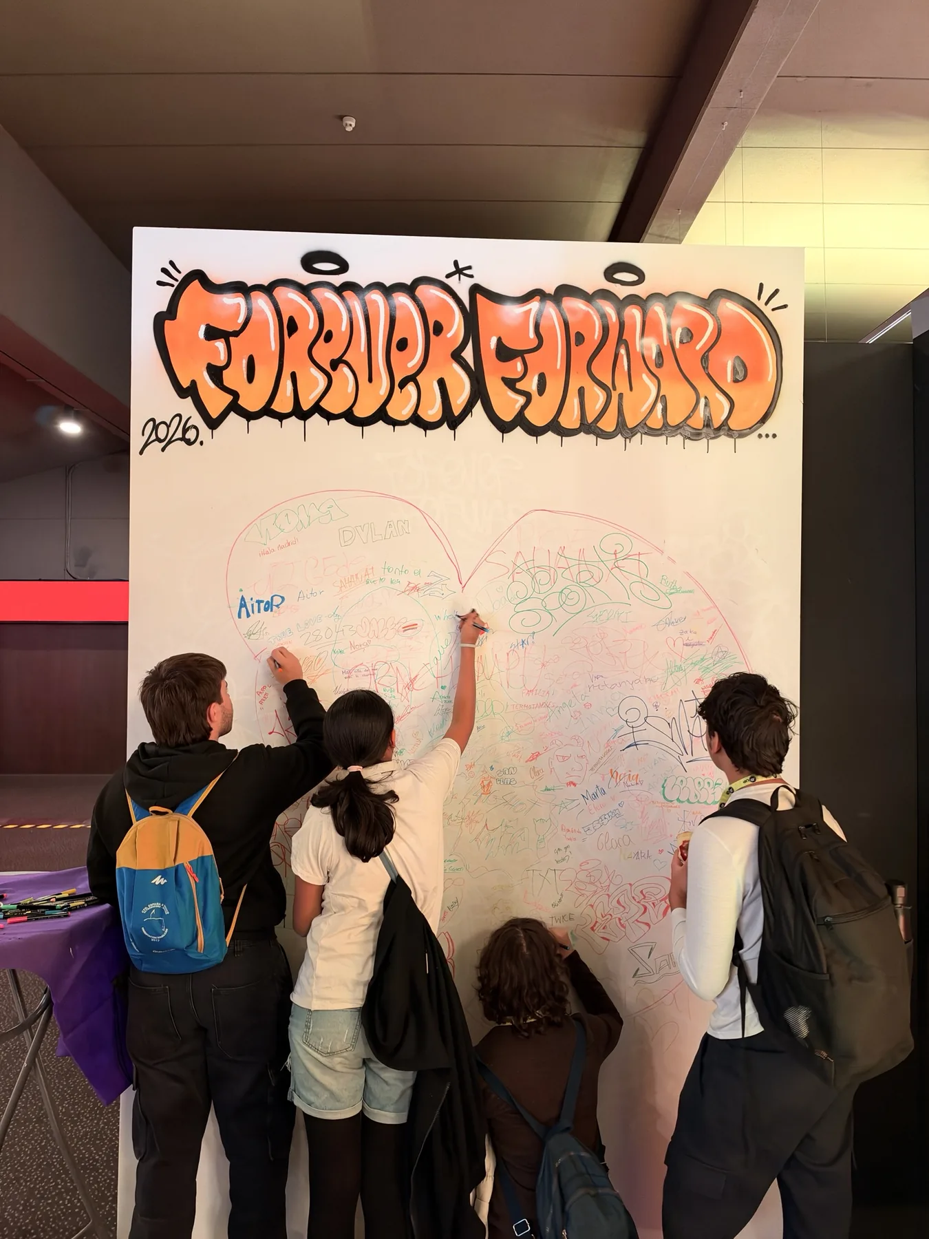 Alumnos firmando con rotuladores de colores dentro del contorno de las letras JD en el lienzo colaborativo de JD Sports.