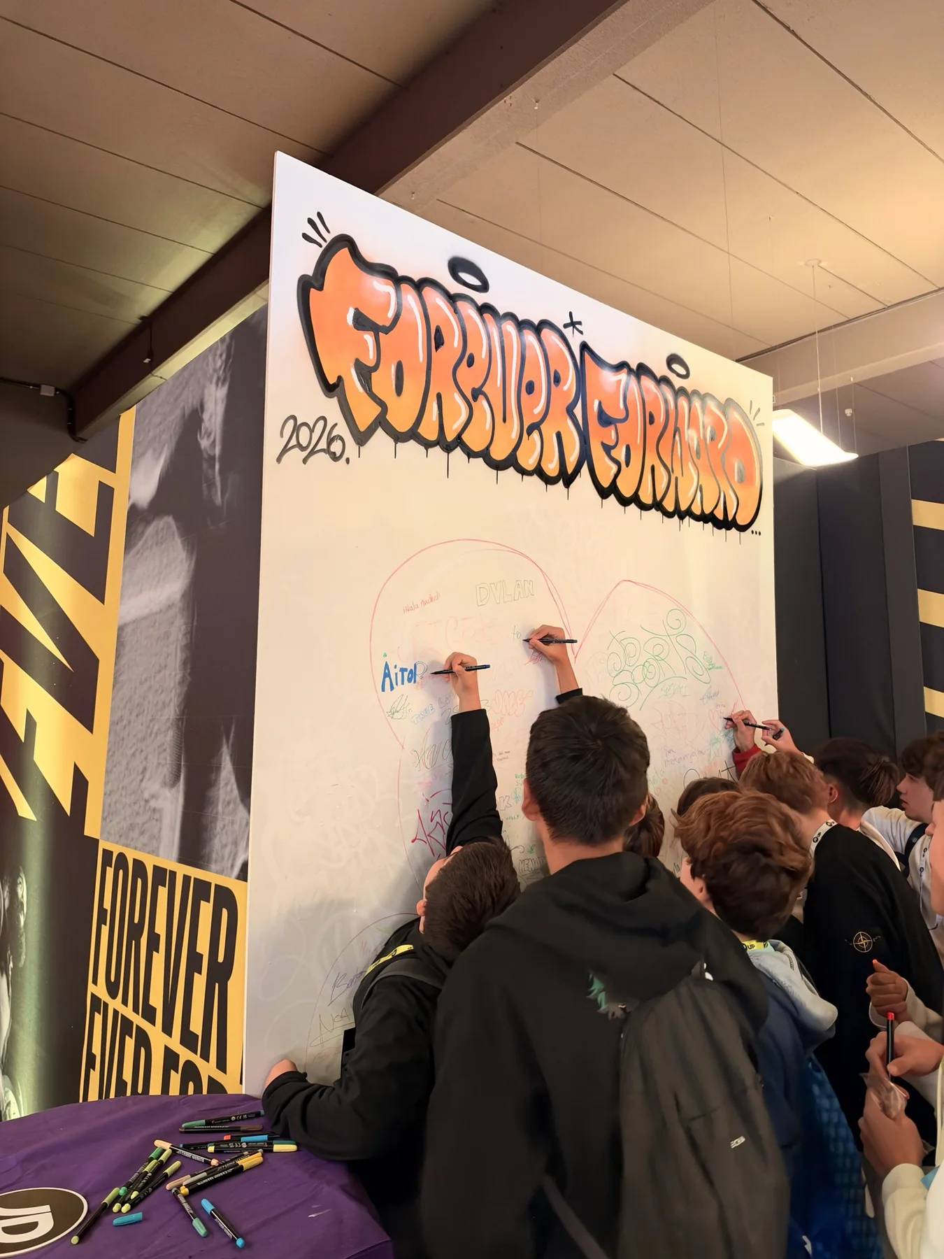 Alumnos dibujando y escribiendo sus nombres en el lienzo colaborativo de JD Sports durante el evento con colegios.