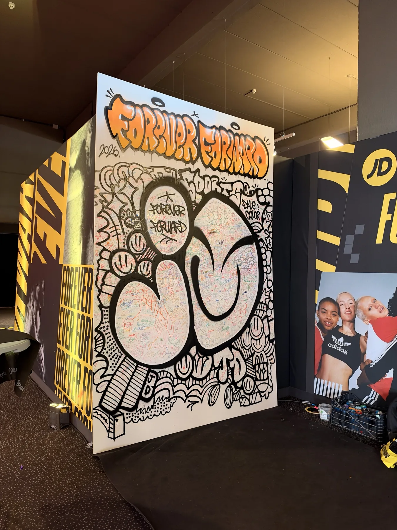 Obra final del lienzo colaborativo de JD Sports: letras JD en negro, caritas, nubes y la firma de Dale Color sobre las firmas de los alumnos.