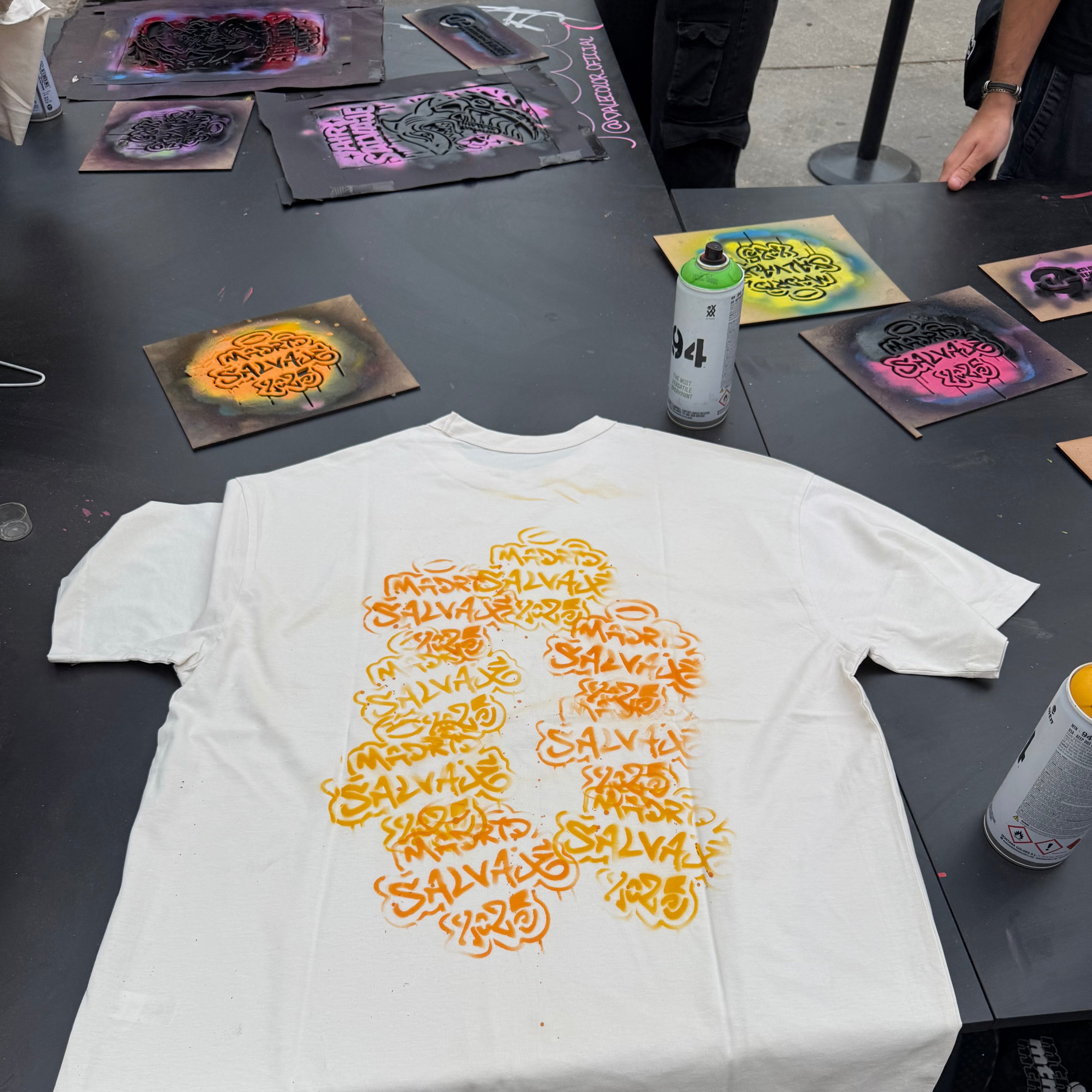 Camiseta blanca personalizada con graffiti naranja mediante técnica de stencil y spray en el stand de JD Sports del festival Madrid Salvaje 2024.