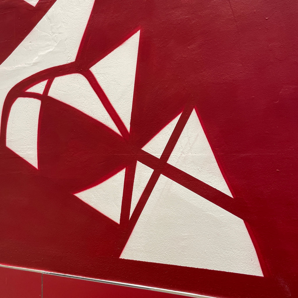 Vista lateral de mural educativo en pared de escalera. Composición cubista con notas musicales, balones y elementos deportivos conectados.