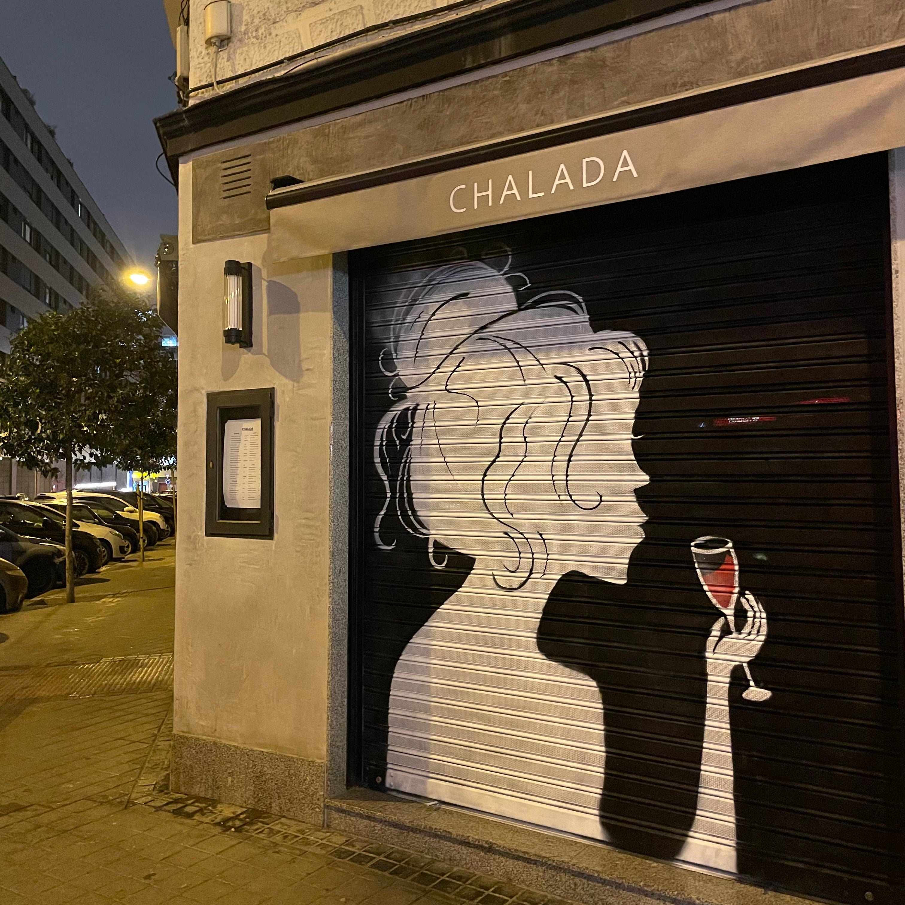 Detalle de pintura mural en cierre: perfil de mujer con peinado despeinado estilo chalada y copa de vino tinto.