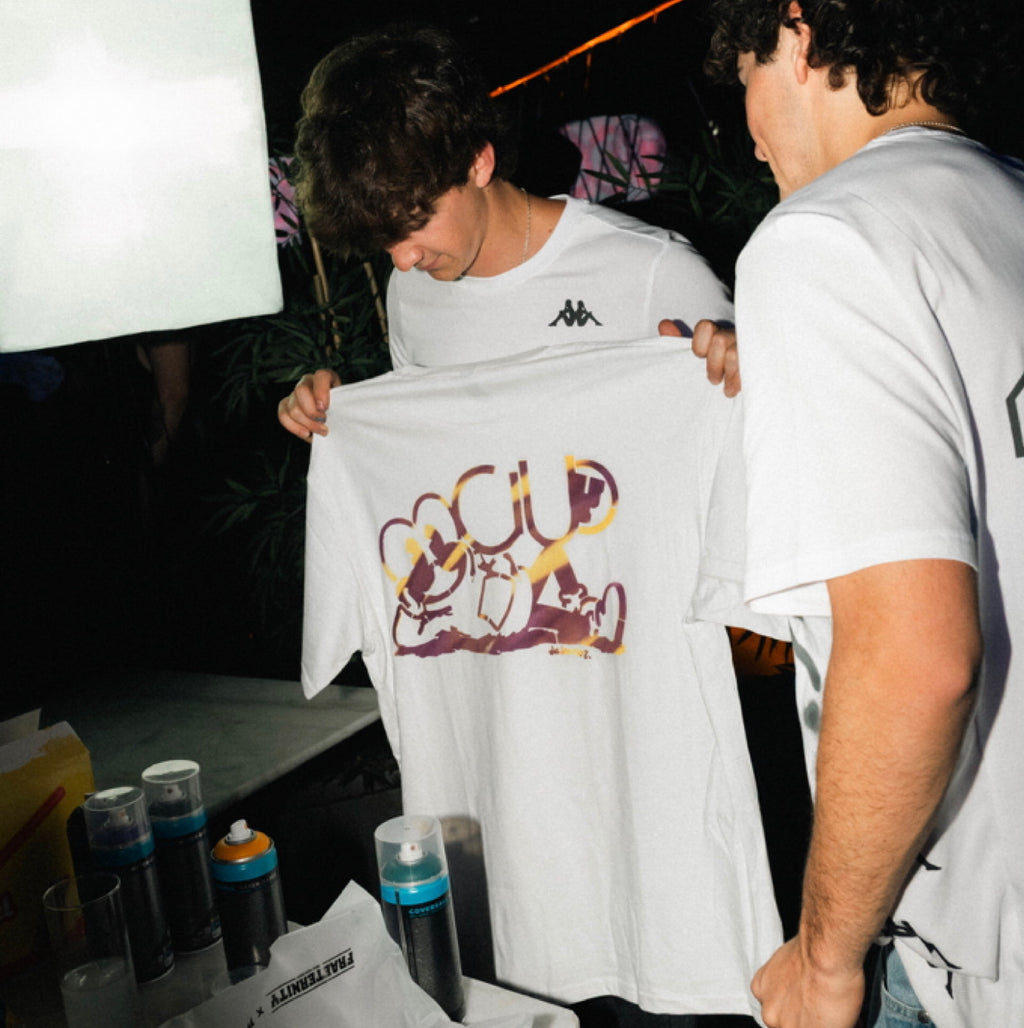 Graffitero profesional en Madrid mostrando el resultado de una camiseta personalizada con spray morado y amarillo para la marca Fraeternity.