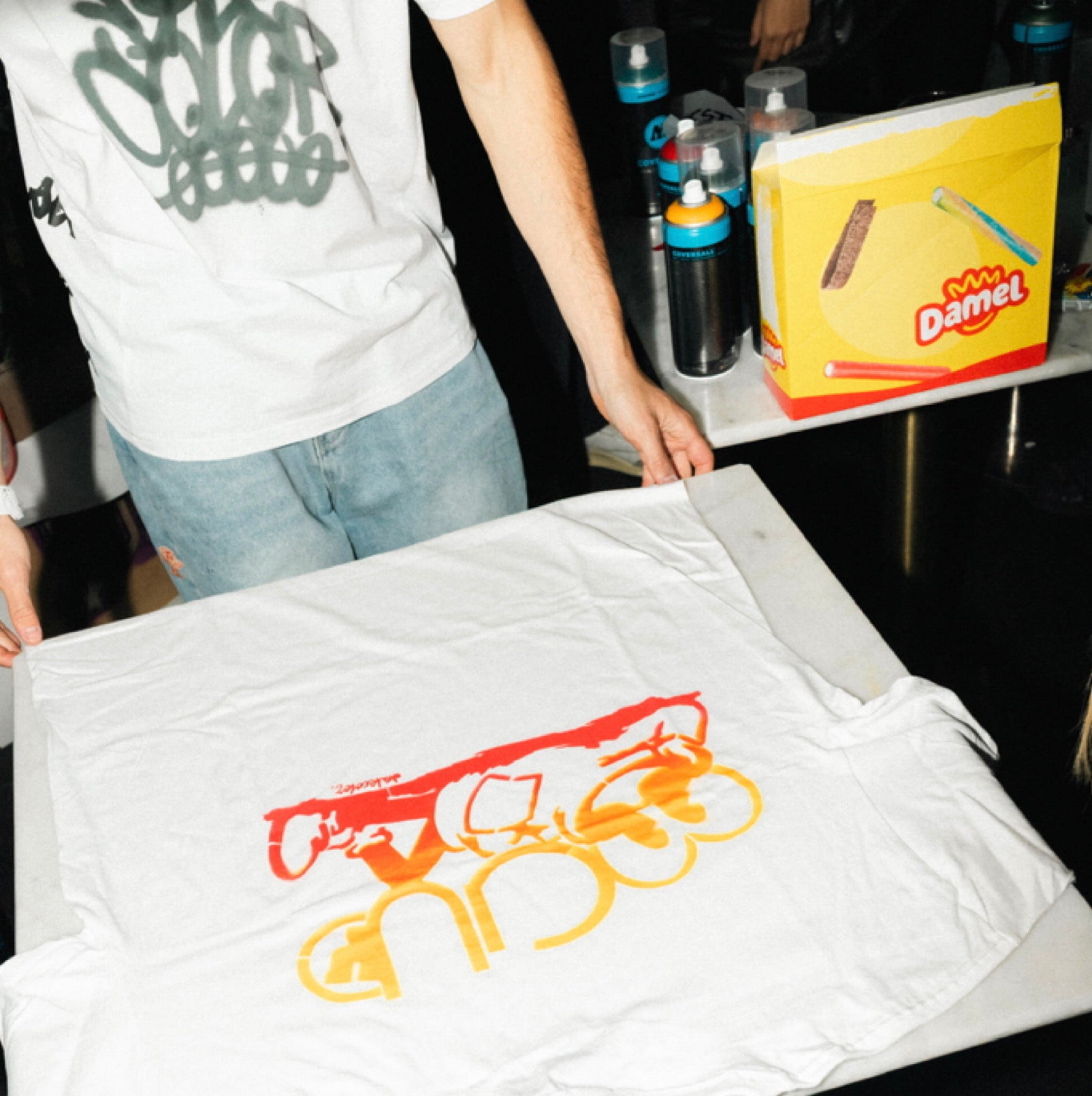 Graffiti para negocios en Madrid. Camiseta con el logotipo de Fraeternity pintada a mano con spray apoyada sobre mesa en el stand de Dale Color en evento privado.