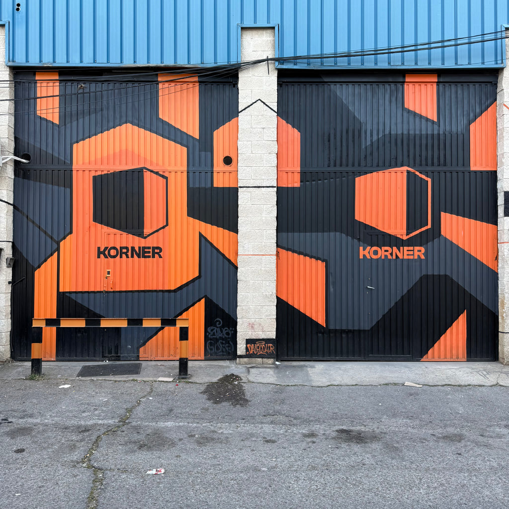 Mural exterior en Madrid. Cierres metálicos de nave industrial pintados a mano con graffiti geométrico naranja y negro para Estudios Korner.
