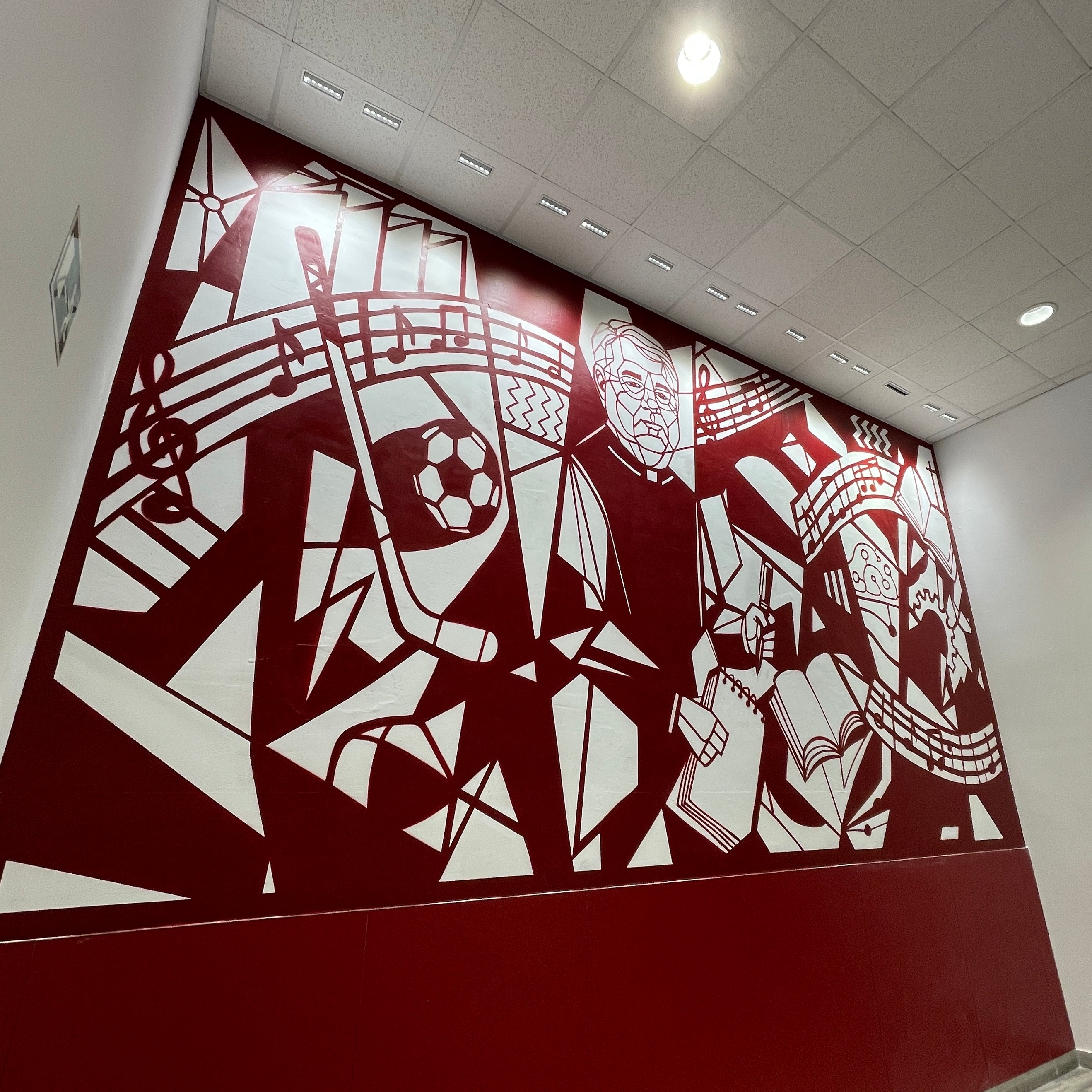 Mural interior en colegio color granate y blanco. Diseño geométrico estilo Guernica con figura de D. Luis rodeado de símbolos educativos.