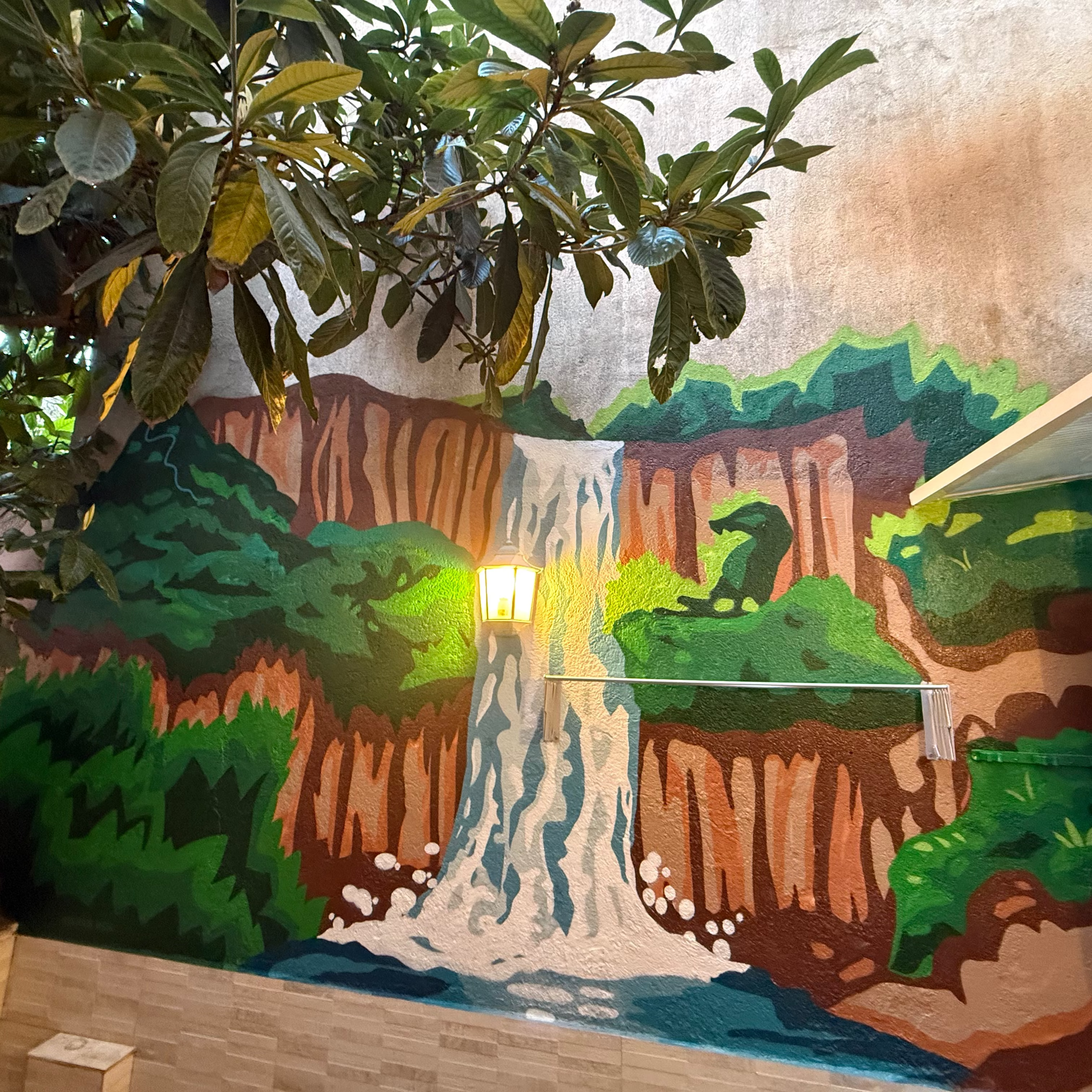 Resultado final de servicio de murales a domicilio en Madrid. Paisaje de naturaleza con cascada integrada al farolillo y árbol real en patio particular.
