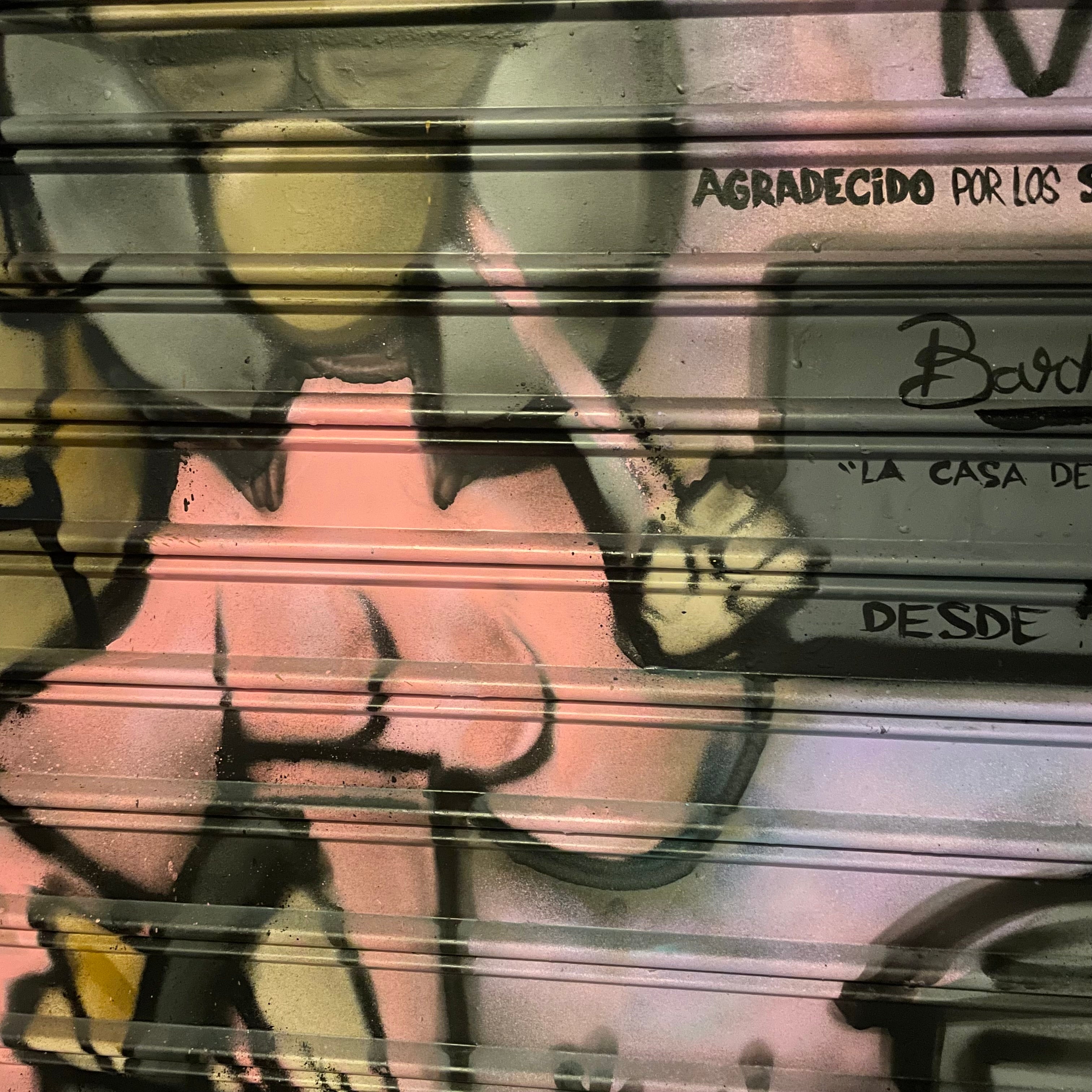 Detalle de pintura mural reinterpretando la placa del Ayuntamiento de Madrid para comercios centenarios. Figuras goyescas a color sobre cierre metálico.