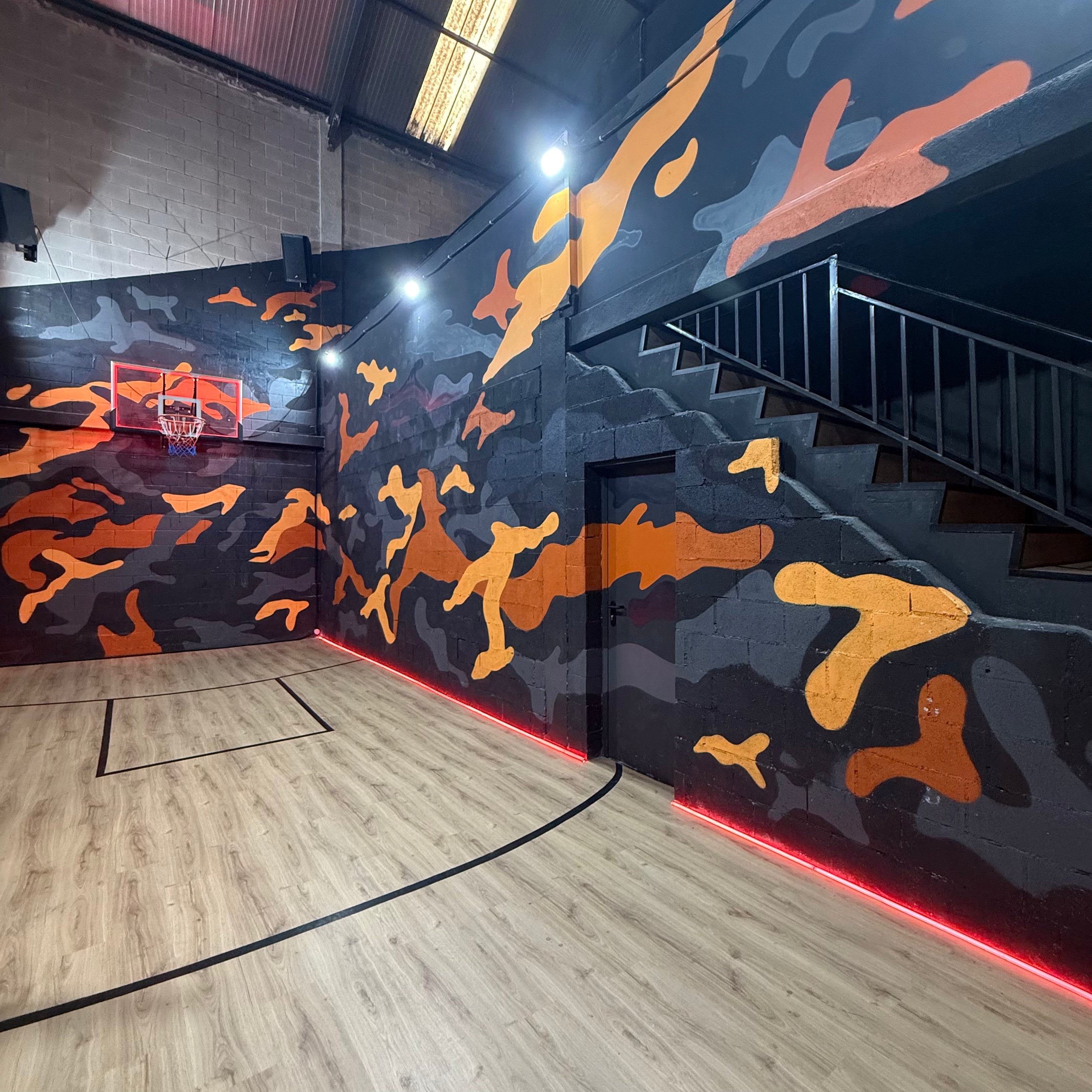 Pintores de graffiti en Madrid decorando el interior de un estudio de música. Cancha de baloncesto con pintura mural de camuflaje naranja y gris.