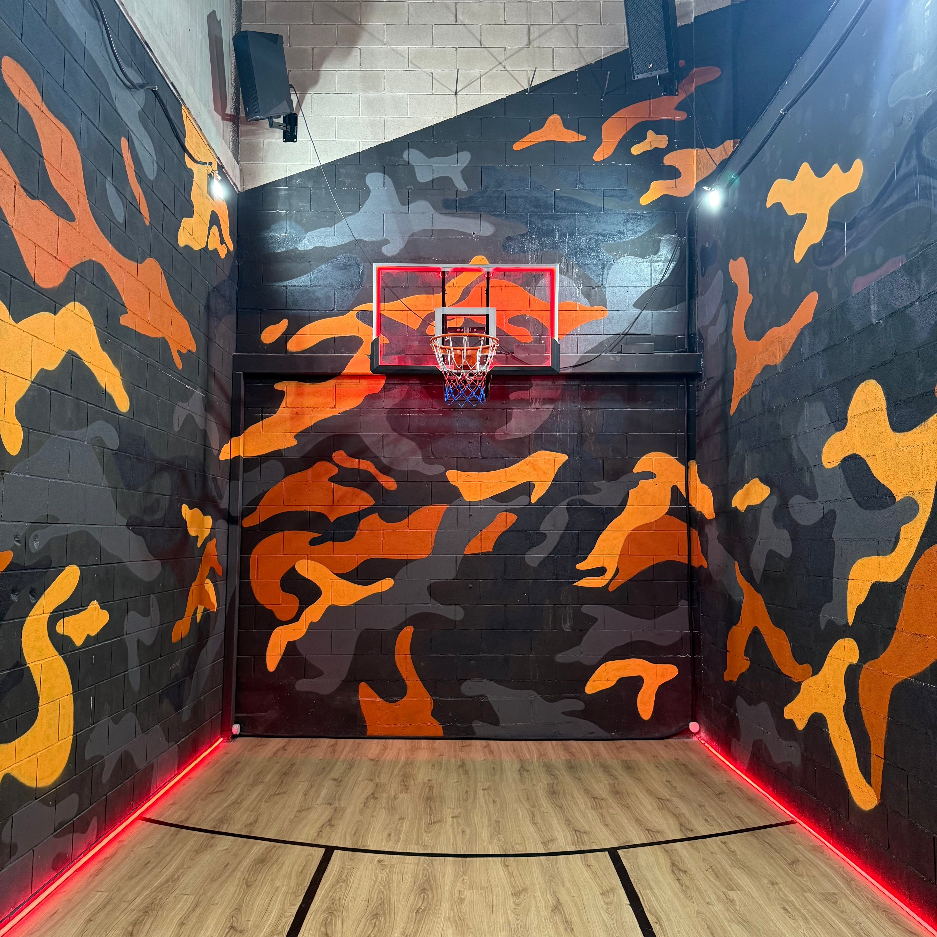 Pintores de graffiti en Madrid decorando el interior de un estudio de música. Cancha de baloncesto con pintura mural de camuflaje naranja y gris.