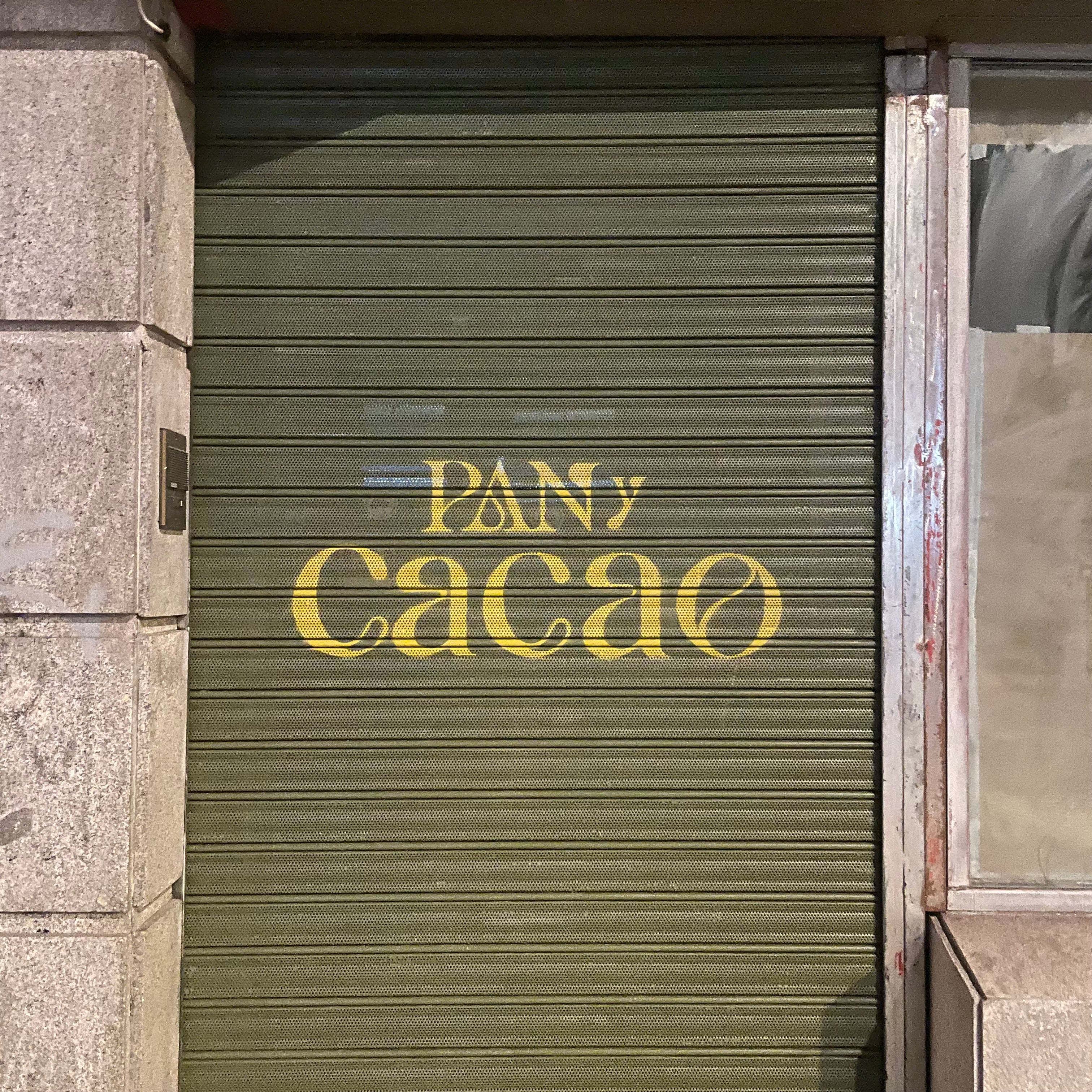 Logotipo Pan y Cacao pintado con plantilla sobre cierre metálico verde. Letras doradas tipografía clásica para panadería en Madrid.
